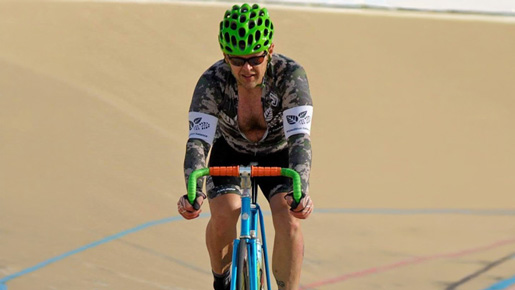 Walter in a velodrome, wearing a cycling kit and helmet, riding a fixed gear track bike